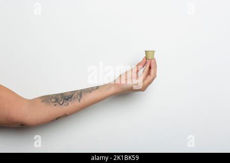 Nahaufnahme`s Arm und Hand einer tätowierten Frau mit einer Kaffeekapsel vor weißem Hintergrund Stockfoto